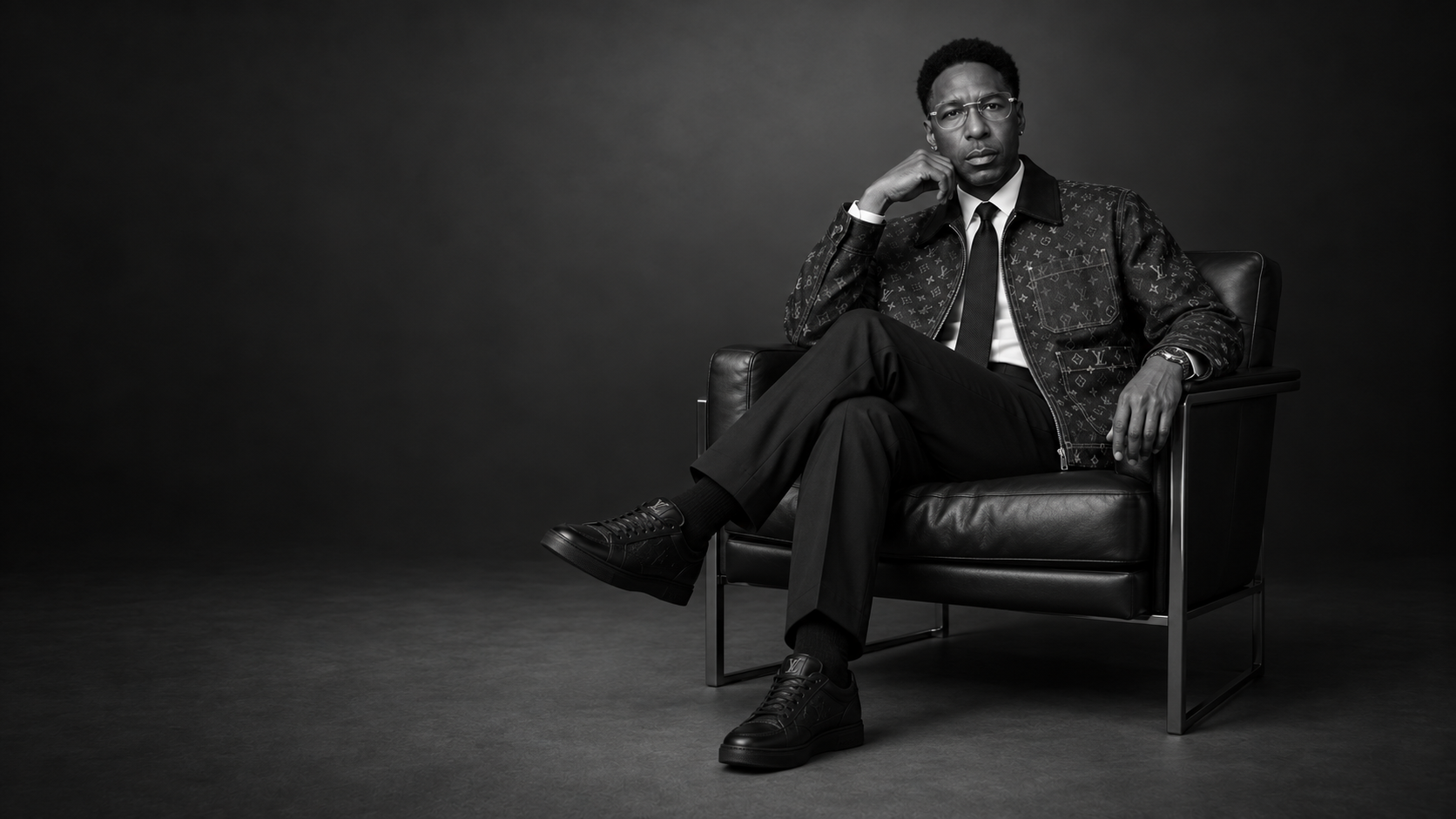 Black-and-white portrait of Lajuane Torrey seated in a black leather armchair, wearing a patterned jacket and tie.